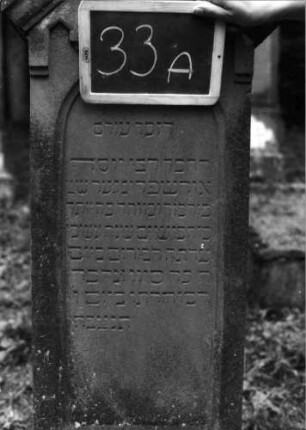 Grabstein 33 (Index: 100090829) Material: Sandstein Zustand: Sockel leicht verwittert Maße HxBxT: 152x41x22 cm Beschreibung: getreppt. Sock. , giebelart. Abschl. m. Verdach. , Schriftfeld m. Rundbogen, Stele Symbolik: gestelztes giebelartiges Fries: Grabstein 33A