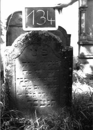 Grabstein 134 (Index: 100103465) Material: Sandstein Zustand: leicht verwittert Maße HxBxT: 80x49x9 cm Beschreibung: Stele, eingezogener Rundbogenabschluss, Schriftfeld eingetieft mit Konvexbogenabschluss: Grabstein 134