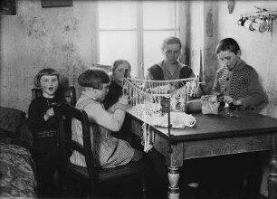 Heimarbeiterin und Kinder beim Posamentieren von Perlfransen für Lampenschirme : Heimarbeiterin und Kinder beim Posamentieren von Perlfransen für Lampenschirme