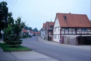 Straßenkreuzung, kleine Freifläche mit Grünanlage; Dorfstraße mit Häusern