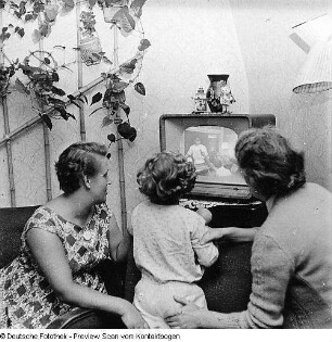 Zwei Frauen mit Kind vor laufendem Fernsehgerät sitzend
