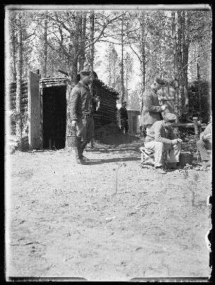 Unbekannte Gegend [Litauen/Weißrussland/Ukraine?]: Soldaten beim Kartoffelschälen neben niedrigen Holzunterständen in einem lichten Wald