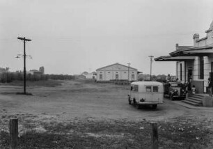 Bahnhofsvorplatz in Mirassol : Der Bahnhofsvorplatz in Mirassol mit dem Bahnhofsgebäude, einem Kaffee und einem Lagerhaus. Vor der Gebäude steht der Bus der Expedition und ein weiteres Fahrzeug, links beginnt die Bahnhofsstraße.