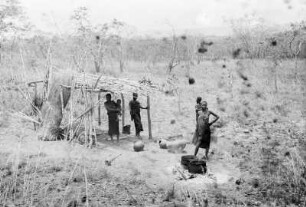 Beim Pombe kochen : Frauen an einem Unterstand in einer Savannenlandschaft beim Pombe kochen