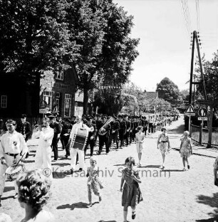 Grönwohld: Amtsfeuerwehrfest des Amtes Lütjensee: Festumzug: Poststraße: rechts Abzweigung der Bahnhofstraße Richtung Lütjensee: vorn links Spielmannszug: dahinter Feuerwehrkapelle:vorn rechts Kinder: hinten links Lebensmittelgeschaft Heinrich Schippmann mit Bäumen: hinten rechts weitere Häuser und Bäume