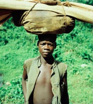Bechem (Ghana). Portrait eines jungen Mannes, eine Last tragend