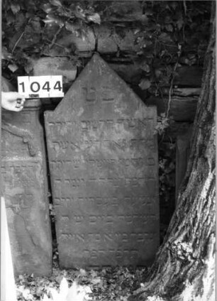 Grabstein 1044 (Index: 99630547) Material: Sandstein Zustand: leicht verwittert, unten eingesunken Maße HxBxT: 121x57x7 cm Beschreibung: Stele mit eingezogenem giebelartigem Abschluß: Grabstein 1044