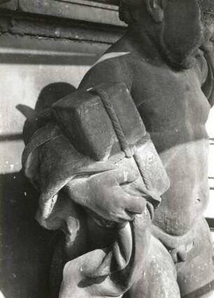 Putto mit Päckchen und Geldbeutel. Um 1905. Sandstein. Figur auf dem Ständehaus, Detail Arm mit Päckchen während der Substanzsicherung/Wiederaufbau Dach. Dresden-Altstadt, Schloßplatz 1