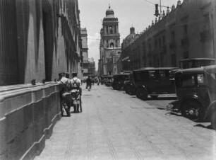 Kathedrale von Mexiko-Stadt : Eine Straße mit parkenden Autos. Links im Bild Polizisten vor einem Seiteneingang des Palacio National; im Hintergrund die Kathedrale von Mexiko-Stadt.