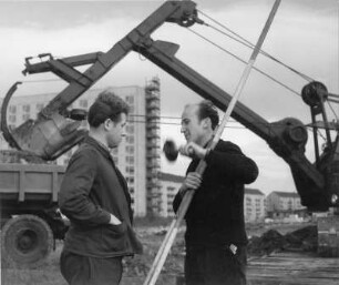 Dresden. Ausleger eines Baggers, davor zwei Bauarbeiter (Vermesser?) im Gespräch