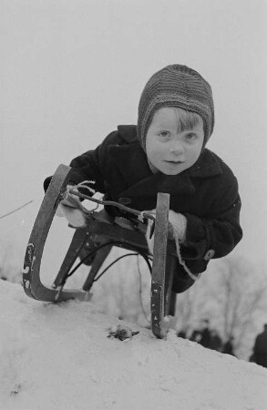 Leipzig, Johannapark. Kinder beim Ski- und Schlittenfahren im Johannapark in Leipzig, Kind auf einem Schlitten liegen kurz vor der Abfahrt