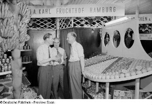 Messestand mit Südfrüchten : Drei Männer umgeben von Südfrüchten auf dm Messestand J. A. Kahl Fruchthof Hamburg der Leipziger Herbstmesse 1954