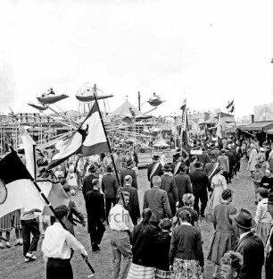 Schützenfest: Veranstalter Bürgerschützengilde von 1627 e.V. Bad Oldesloe: Umzug: Einmarsch auf Festplatz an Sehmsdorfer Straße: Schützenvereine marschieren mit Fahnen und Gästen [Rückenansicht], im Vordergrund Jugendliche mit Fahnen der Landsmannschaften [Rückenansicht]: zu beiden Seiten Zuschauer mit Kindern: hinten Raketen-Karussell in Fahrt, Jahrmarktstände, 28. Juni 1959