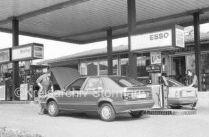 Sandesneben (Kreis Herzogtum Lauenburg): Tankstelle Esso-Station Osterhoff: Hauptstraße, bei Abzweig Blumenstraße: an Zapfsäulen: Serviceleiter Thomas Elsler bei Blick in Motorraum von Pkw: rechts Kunde an Pkw: 14. April 1989