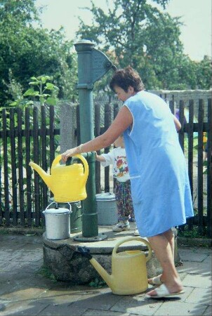 beim Kindergarten: Frau mit Kind beim Wasserholen an einer Pumpe