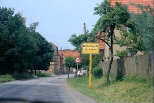 steile Dorfstraße mit Ortsschild, Straßenrandbegrünung,Obstbäume