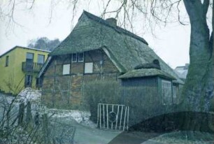 Schulstraße 27: traufständige Fachwerkkate mit Reetdach: Giebelseite: rechts Pavillon mit Reetdach, vorne Hofeinfahrt: im Hintergrund Neubau