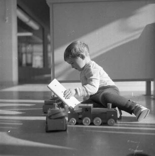 Junge beim Spielen mit einer Holzeisenbahn, aufgenommen wohl im Kunden-Kindergarten eines Einkaufsmarktes
