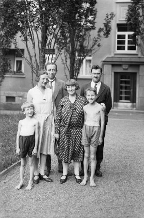 Gruppenaufnahme einer Familie (?) auf dem Weg vor einem Hauseingang