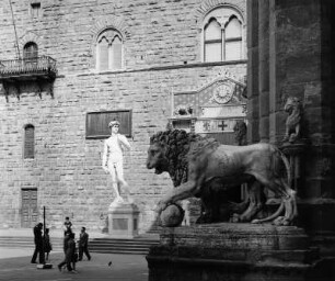 Florenz, Piazza della Signoria. Blick über den Löwen der Loggia dei Lanzi zum David (1501/1504; Michelangelo Buonarroti) vor dem Palazzo Vecchio