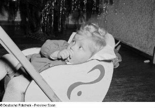 Porträt eines kleinen Mädchens mit Puppenwagen vor einem Weihnachtsbaum