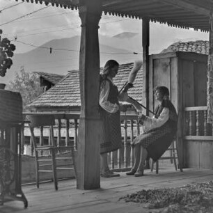 Veranda eines Wohnhauses in Bansko. Zwei junge Frauen in bulgarischer Tracht üben das Handwerk des Spinnens aus