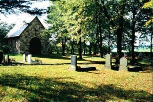 Friedhof mit Gräbern und Bäumen; hinten Leichenhalle (?)