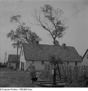 Häuser mit Brunnen mit Handschwengelpumpe und Frau