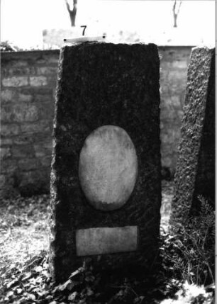 Grabstein 7 (Index: 100081786) Material: Granit, weiße Marmorplatten Zustand: Schriftplatten verwittert Maße HxBxT: 156x60x27 cm Beschreibung: konische Stele, gerader Abschluß, ovale und querrechteckige Schriftplatte: Grabstein 7