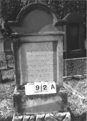 Grabstein 92 (Index: 99609728) Material: Sandstein Zustand: verwittert Maße HxBxT: 170x63x31 cm Beschreibung: Stele, eingezogener Rundbogenabschluß mit Verdachung, Mittelpalmette, Schriftfeld rechteckig eingetieft, getreppter Sockel, unten Rusticaimitat: Grabstein 92A