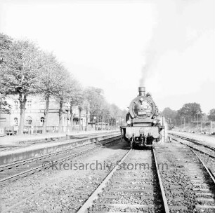 Bahnhofsgelände: Gleise mit Dampflokomotive: links Bahnsteige, Wasserkran, Baumreihe, Bahnhofsgebäude: Blick nach Norden