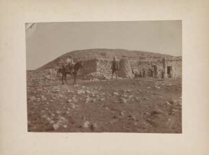 Hugo Grothe zu Pferd : Expeditionsleiter und Geograph Hugo Grothe (1869-1954) auf dem Pferd. Neben ihm ein Mann, im Hintergrund Bewohner vor einem Haus.