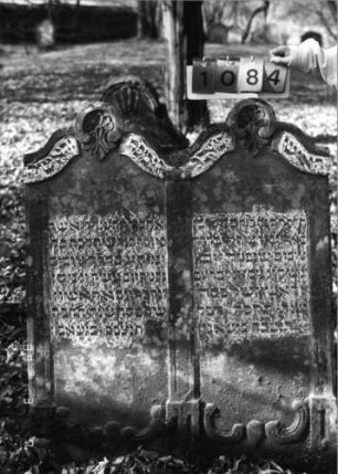 Grabstein 1084 (Index: 99753307) Material: Sandstein Zustand: leicht verwittert Maße HxBxT: 131x104x15 cm Beschreibung: Doppelstele, zwei Schriftfelder eingetieft Symbolik: zwei Muscheln, Blätter: Grabstein 1084