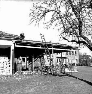 Volksschule am Schweinemarkt [später Emil-Nolde-Schule]: Erweiterungsbau: Anbau an Pausenhalle in Bau: Leiter, Zementsäcke, Arbeiter: vorne rechts Baum: im Hintergrund Klassentrakt