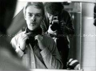 Ein Mann, der sich ein Halstuch bindet, im Hintergrund der Fotograf, beides im Spiegel zu sehen (Altersgruppe 14-17)