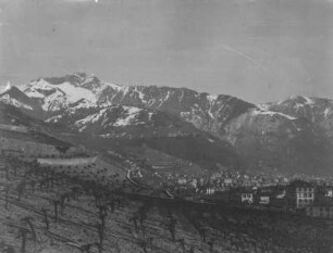 Stadt im Gebirge : Panoramablick auf schneebedeckte Berggipfel, im Vordergrund eine Stadt mit Weinberg