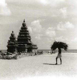 Mahabalipuram, Indien. Zwei der sogenannten Sieben Pagoden, davor Last auf dem Kopf tragender Inder
