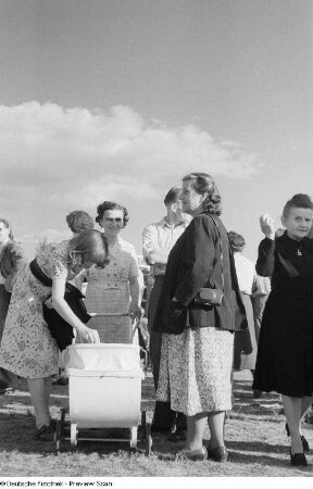 Renate Rössing sowie die Mutter Roger Rössings (mit Fotokameratasche) an einem Kinderwagen, umgeben von einer Vielzahl weiterer Personen