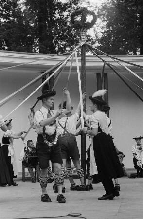 Menschen in Tracht tanzen um einen Maibaum