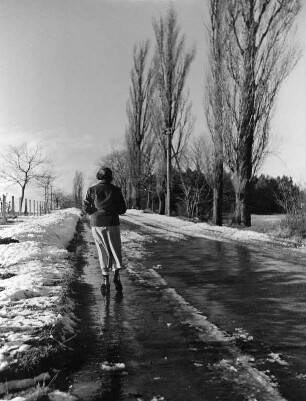 Winterbilder. Restschnee. Fußgängerin auf einer Landstraße