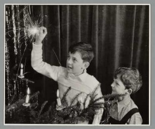 Zwei Jungen mit einer Wunderkerze vor einem Weihnachtsbaum