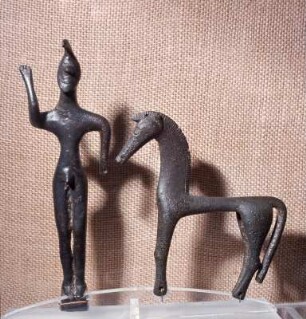 Olympia. Neues Museum. Nachgeometrische Zeus-Statuette, Bronze, 7. Jh. v. Chr.. Rechts daneben Pferdevotiv