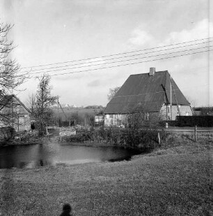 Löschteich mit Rasenfläche und Sträuchern: dahinter Bauernhäuser: im Hintergrund links Siedlungshäuser