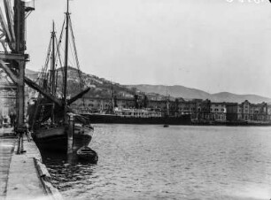 Am Hafen : Blick von einer Anlegestelle auf ein vor Anker liegendes Segeslschiff und den Hafen von Triest.