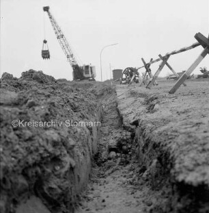 Industriestraße: Absackung eines Teilstücks: in der Mitte Grube: rechts Absperrung, links Erdhaufen: dahinter Bagger, Baubude und Pkw