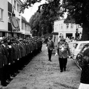 Schützenfest: Veranstalter Schützenverein Reinfeld und Umgebung von 1954 e.V.: Bergstraße (links) / Paul-von-Schoenaich-Straße (hinten): Schützenkönig Eugen Richter und die beiden Ritter Dietmar Kobrow und Herbert Bornhöft schreiten Front der mit Standarte angetretenen Schützen ab: rechts Rathausvorplatz mit Fleckenspumpe, Baum, parkenden Autos: hinten Zuschauer, 4. September 1966