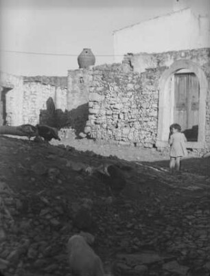 Irdener Rauchabzug : Mädchen und Hühner auf einer Straße; dahinter eine hohe Steinmauer, auf deren First ein Rauchabzug aus Ton zu erkennen ist.