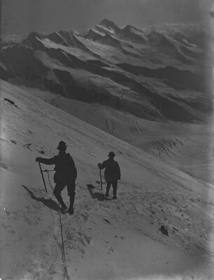 Bergsteiger : Zwei Bergwanderer auf einem beschneiten Wanderweg mit Sicherungsseilen. Im Hintergrund das Finsteraarhorn