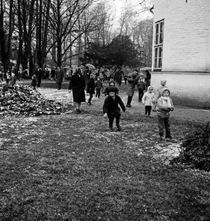 Schlosspark: Ostereiersuchen: Kinder suchen im Regen: Erwachsene mit Regenschirmen: rechts Schloss
