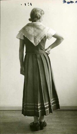 Frau stehend in Volkstracht mit handgewebtem Kleid. Rückseitig. Halbtotale